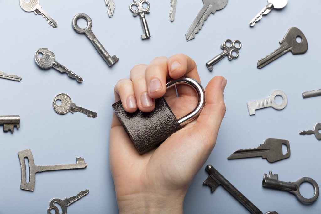 A hand holding a heavy-duty padlock surrounded by various keys on a blue background, representing security solutions and an emergency locksmith near me.